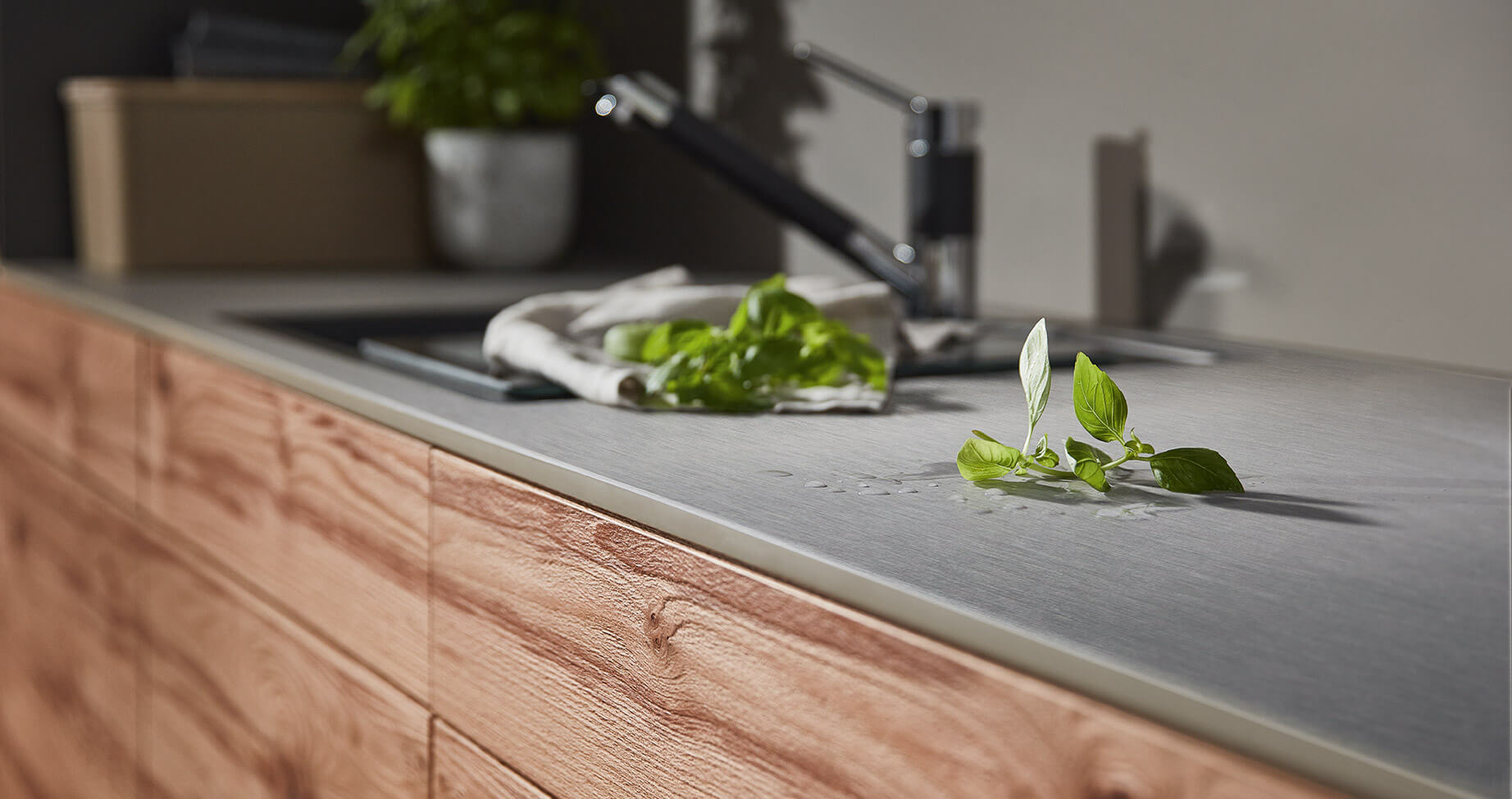 graue Kompaktarbeitsplatte mit eingelassener Spüle, Wassertropfen und Kräuter auf der Platte im Vordergrund