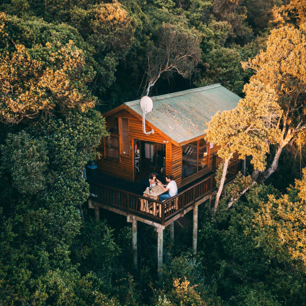 Holzhaus auf Holzständern im Wald, Paar sitzt auf Terrasse